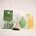 Jasmine snow bud tea packaging set with a large white and green resealable pouch, a smaller flat packet, loose tea leaves, and a glass of brewed tea on a white background.