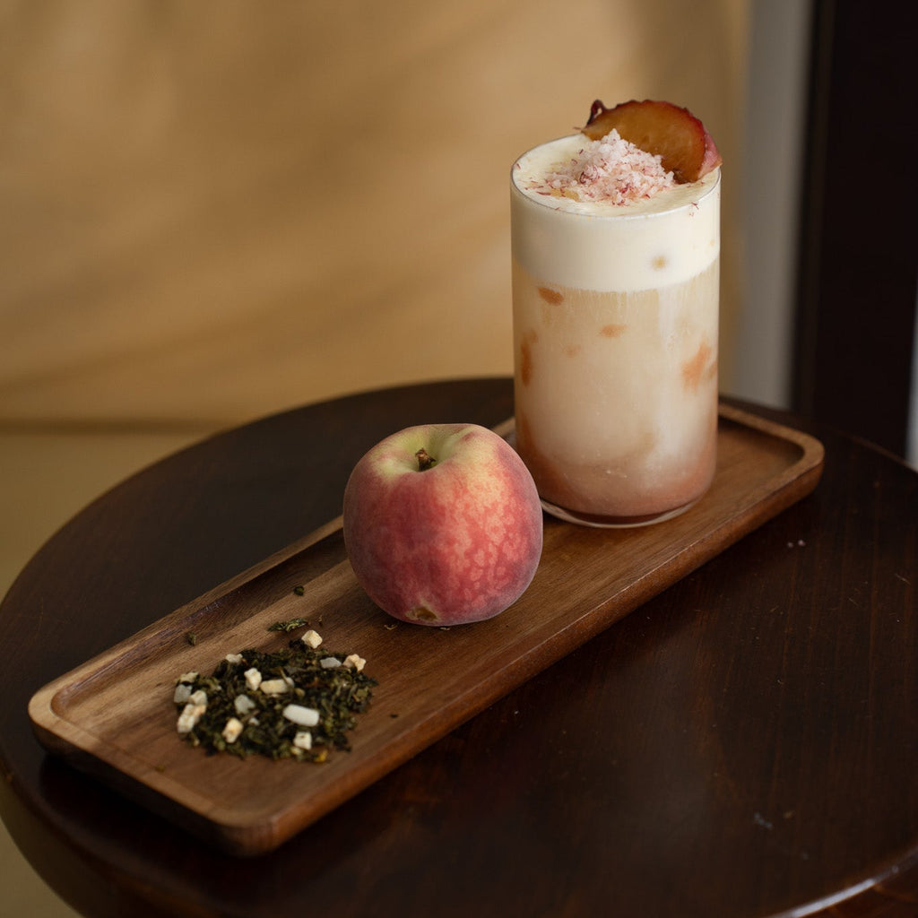 Milk tea with a peach garnish on a wooden tray with a peach and loose leaf tea. 